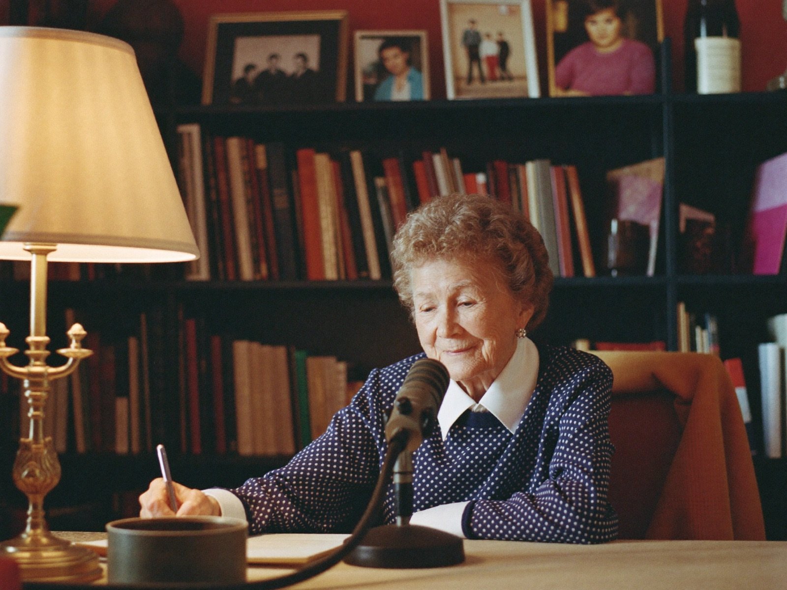 A woman records her life stories at a warm desk with a small microphone.
